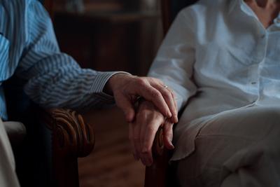 Gros plan sur les mains ridées de deux personnes âgées qui se tiennent l'une l'autre, posées sur leurs avant-bras.