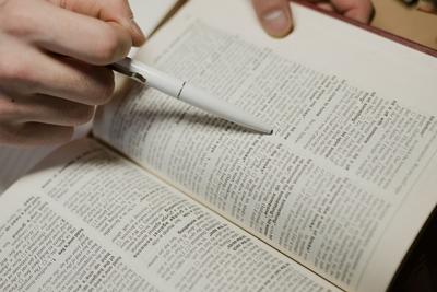 Une main tenant un stylo pointe une définition dans un dictionnaire ouvert.