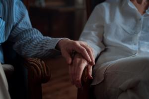 Gros plan sur les mains ridées de deux personnes âgées qui se tiennent l'une l'autre, posées sur leurs avant-bras.