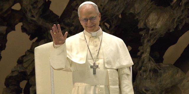 Le pape Léon XIV, vêtu de blanc, lève la main droite pour saluer.