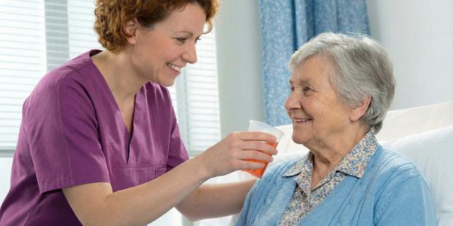 Une soignante donne à boire à une personne en soins palliatifs