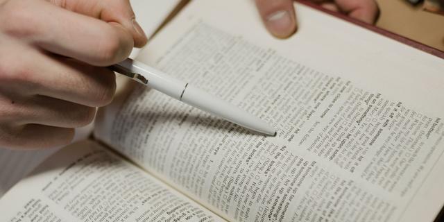 Une main tenant un stylo pointe une définition dans un dictionnaire ouvert.
