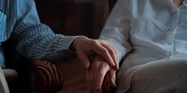 Gros plan sur les mains ridées de deux personnes âgées qui se tiennent l'une l'autre, posées sur leurs avant-bras.