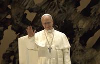 Le pape Léon XIV, vêtu de blanc, lève la main droite pour saluer.