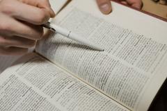 Une main tenant un stylo pointe une définition dans un dictionnaire ouvert.