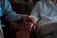 Gros plan sur les mains ridées de deux personnes âgées qui se tiennent l'une l'autre, posées sur leurs avant-bras.