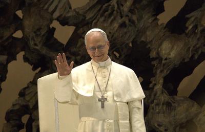 Le pape Léon XIV, vêtu de blanc, lève la main droite pour saluer.